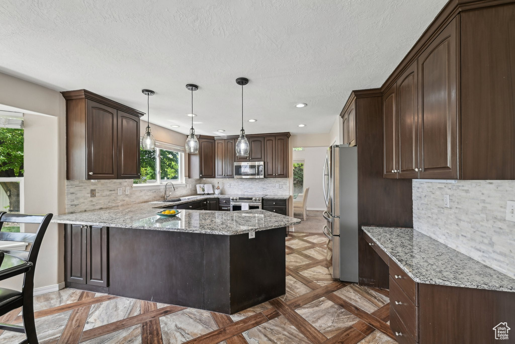Kitchen featuring appliances with stainless steel finishes, a peninsula, dark brown cabinetry, a sink, and backsplash