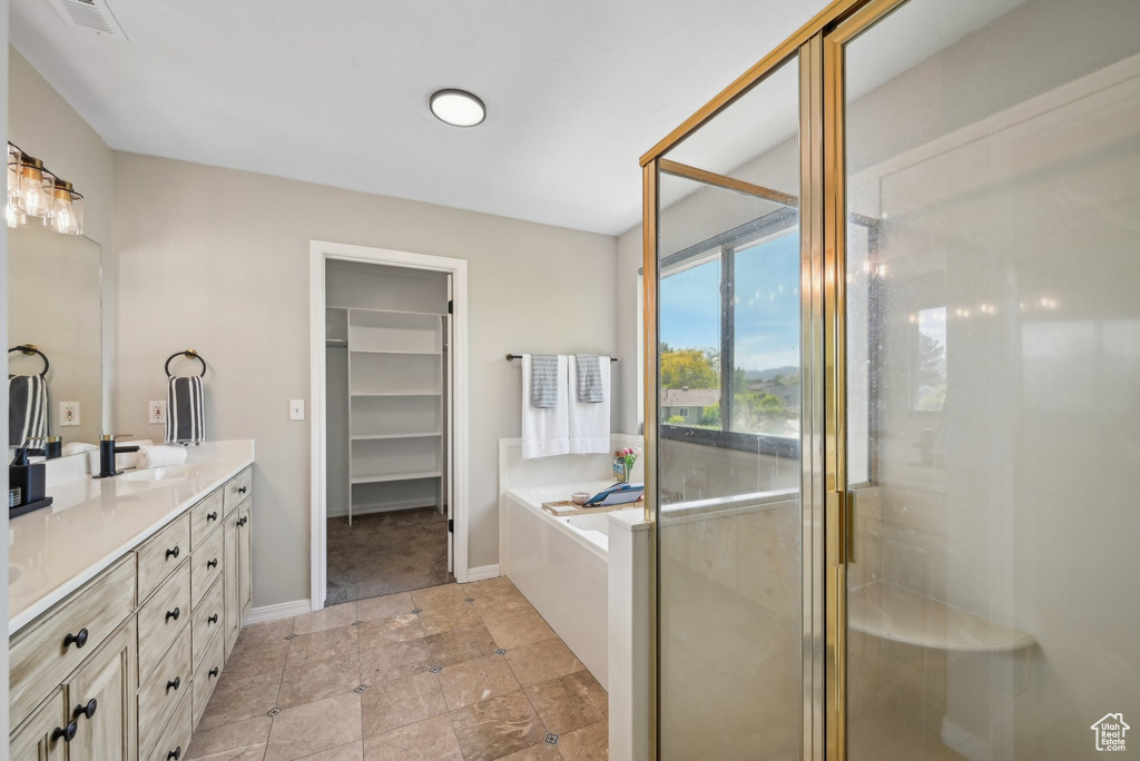 Full bathroom featuring double vanity, a garden tub, a shower stall, a walk in closet, and baseboards