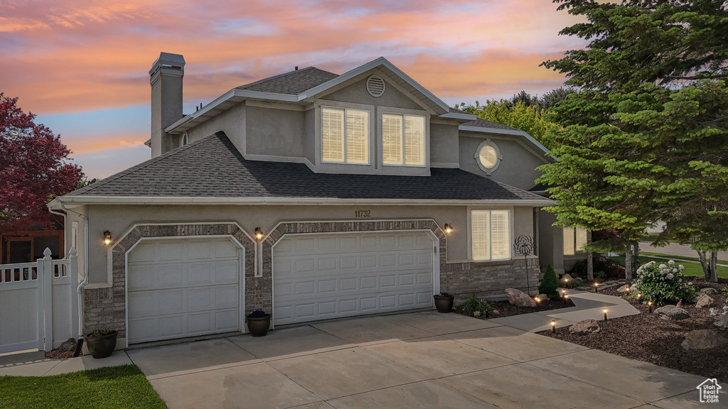 View of front of property with stucco siding, driveway, a chimney, roof with shingles, and an attached garage