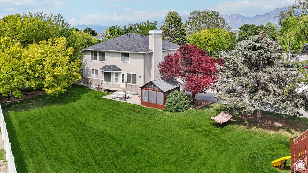 Back of property with a patio area, stucco siding, a yard, roof with shingles, and a chimney