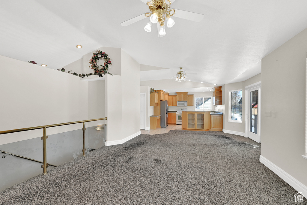 Unfurnished living room with light colored carpet, vaulted ceiling, baseboards, and ceiling fan