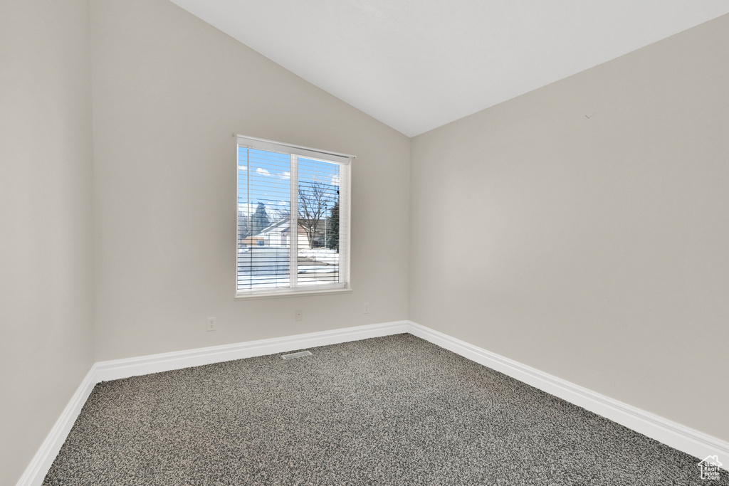 Unfurnished room featuring lofted ceiling, baseboards, visible vents, and dark colored carpet