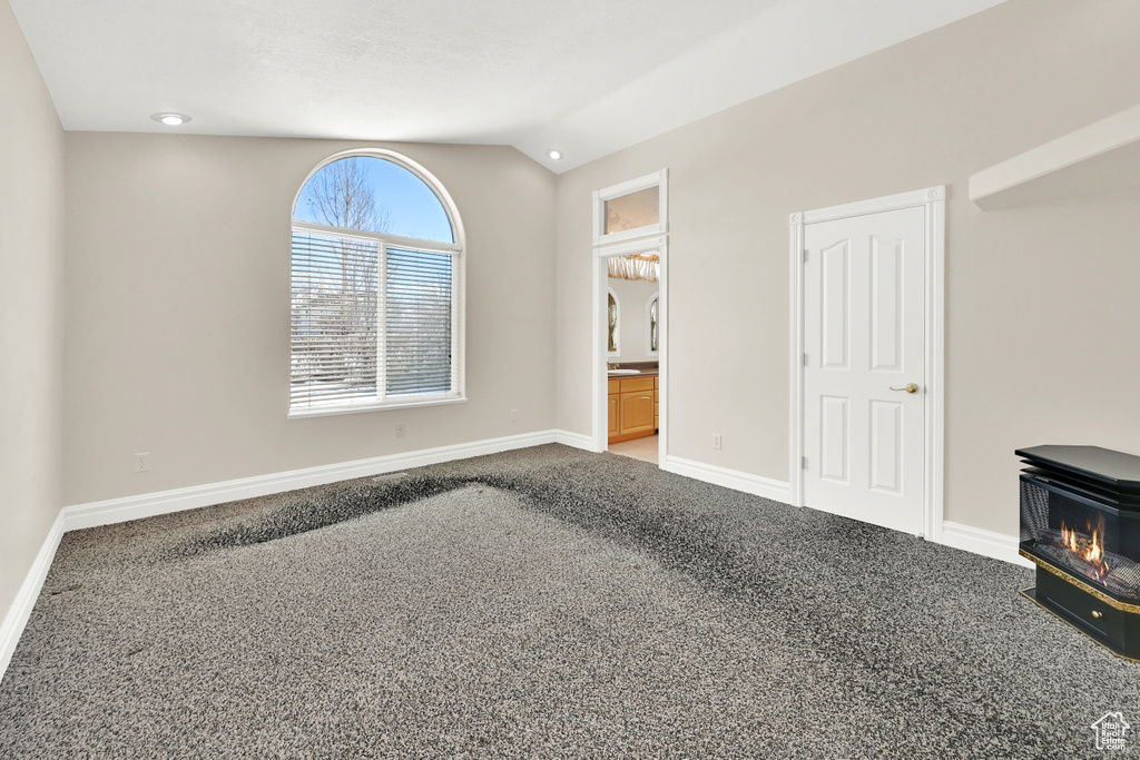 Unfurnished bedroom featuring lofted ceiling, carpet flooring, a wood stove, and baseboards
