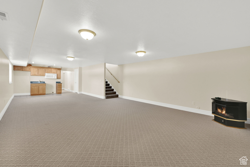 Finished basement with baseboards, stairway, visible vents, and light colored carpet