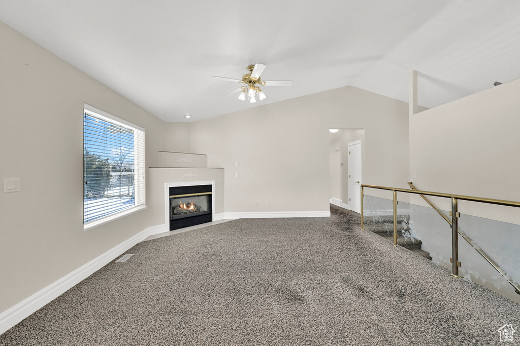 Unfurnished living room featuring carpet, lofted ceiling, visible vents, a fireplace with flush hearth, and baseboards