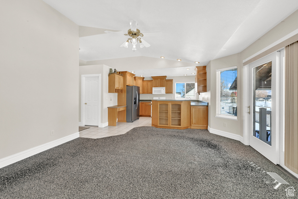 Kitchen with open shelves, lofted ceiling, light colored carpet, white microwave, and stainless steel fridge