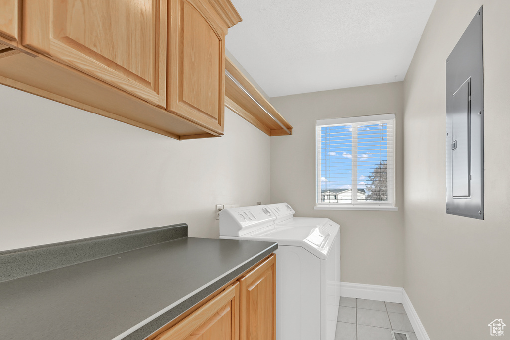 Washroom featuring cabinet space, light tile patterned floors, electric panel, baseboards, and washer and dryer