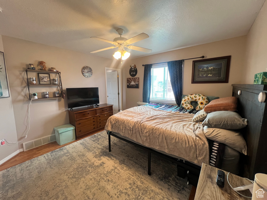 Bedroom featuring a textured ceiling, wood finished floors, a ceiling fan, visible vents, and baseboards