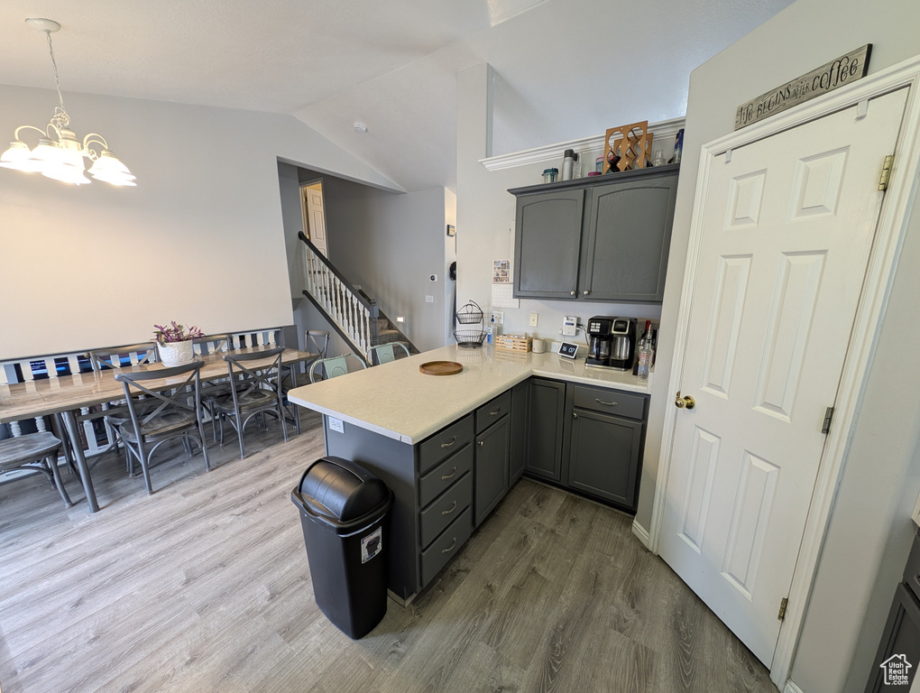 Kitchen featuring vaulted ceiling, a peninsula, wood finished floors, and light countertops