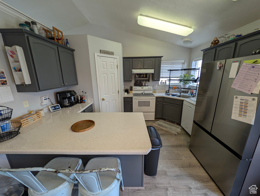 Kitchen featuring white appliances, light countertops, vaulted ceiling, and a peninsula