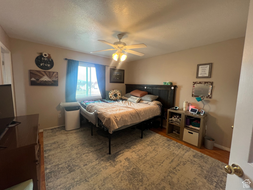 Bedroom with a textured ceiling, wood finished floors, a ceiling fan, and baseboards
