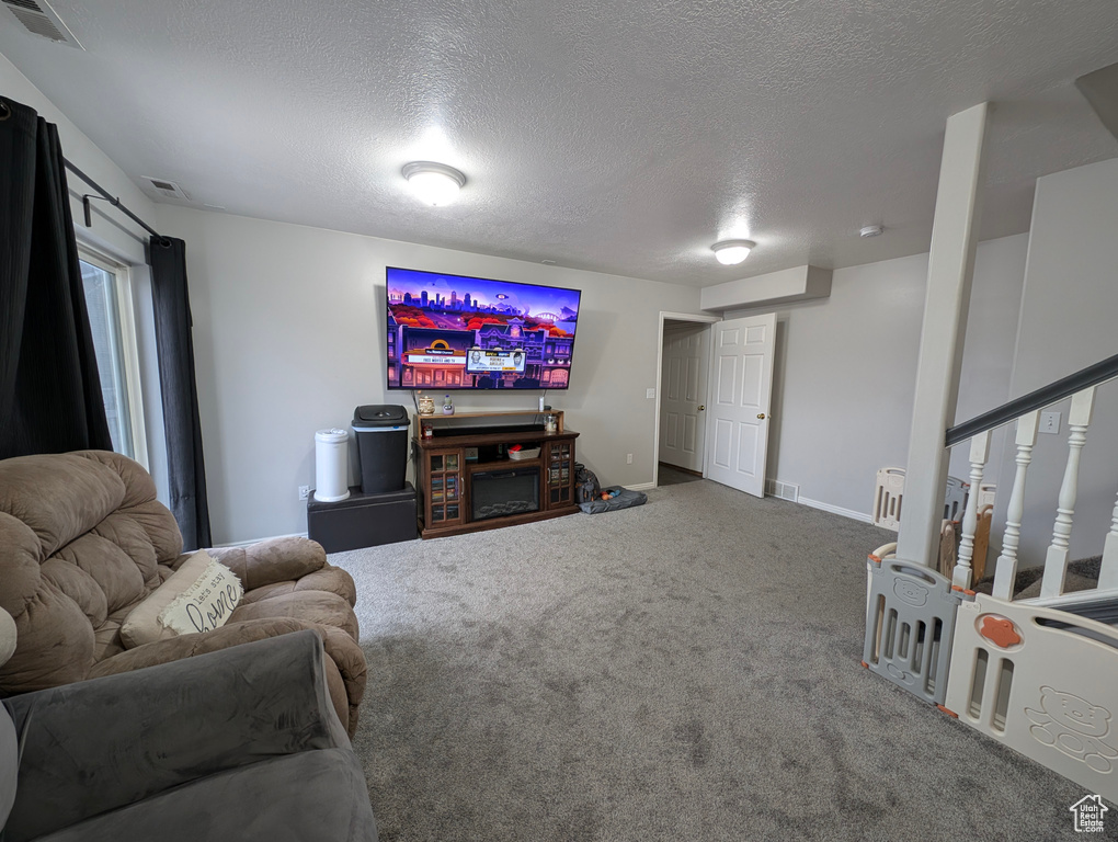 Living area with stairs, a textured ceiling, visible vents, and carpet flooring