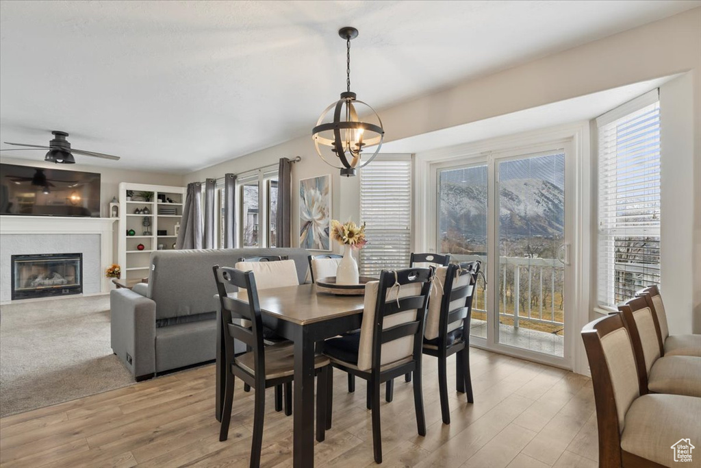 Dining area featuring a glass covered fireplace, light wood finished floors, and ceiling fan with notable chandelier