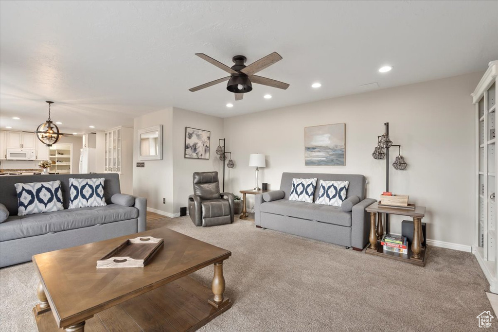 Carpeted living area with ceiling fan with notable chandelier, baseboards, and recessed lighting