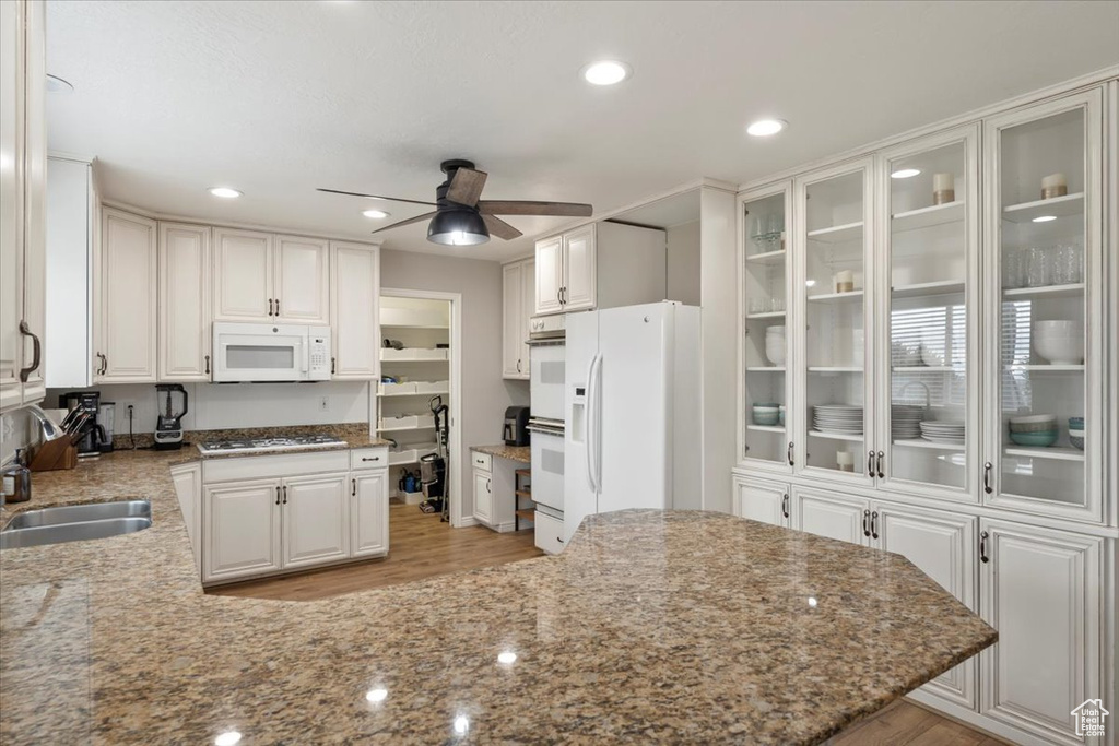 Kitchen featuring white appliances, a sink, a ceiling fan, and light stone countertops