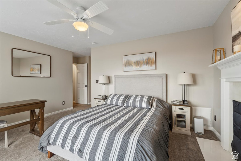 Carpeted bedroom featuring a fireplace with flush hearth, baseboards, and a ceiling fan