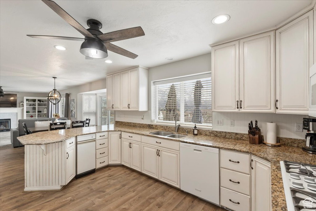 Kitchen with ceiling fan, a peninsula, white appliances, a sink, and a glass covered fireplace