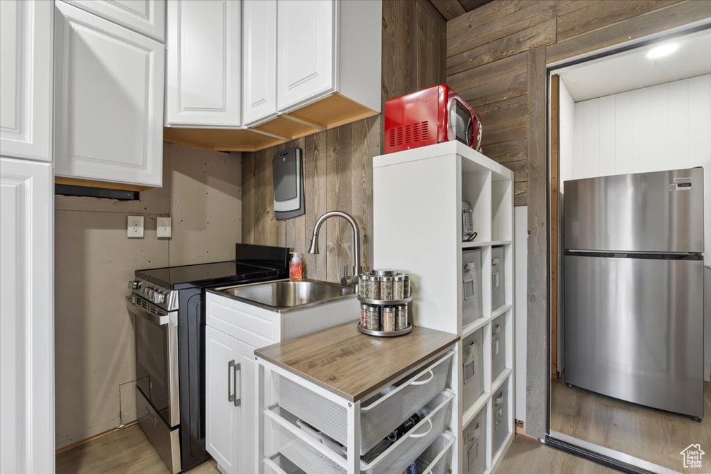 Kitchen with stainless steel appliances, white cabinetry, a sink, wooden walls, and light wood-type flooring