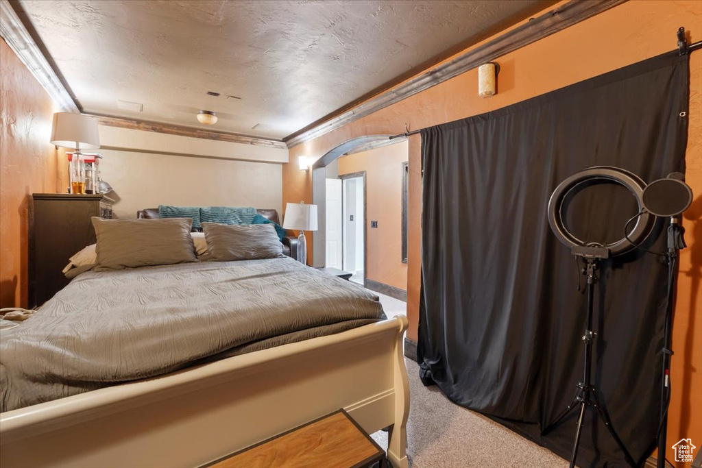 Carpeted bedroom with arched walkways, crown molding, and a textured ceiling