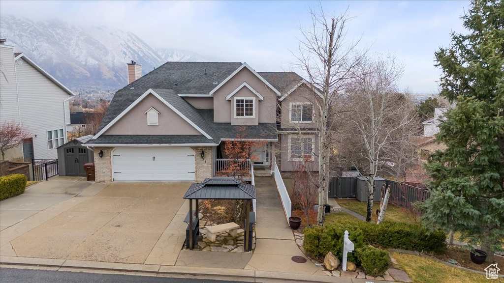 Traditional home with brick siding, a shingled roof, concrete driveway, fence, and a mountain view