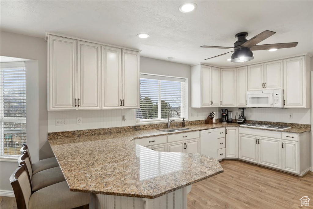 Kitchen featuring a peninsula, white appliances, a breakfast bar, a sink, and light wood-type flooring