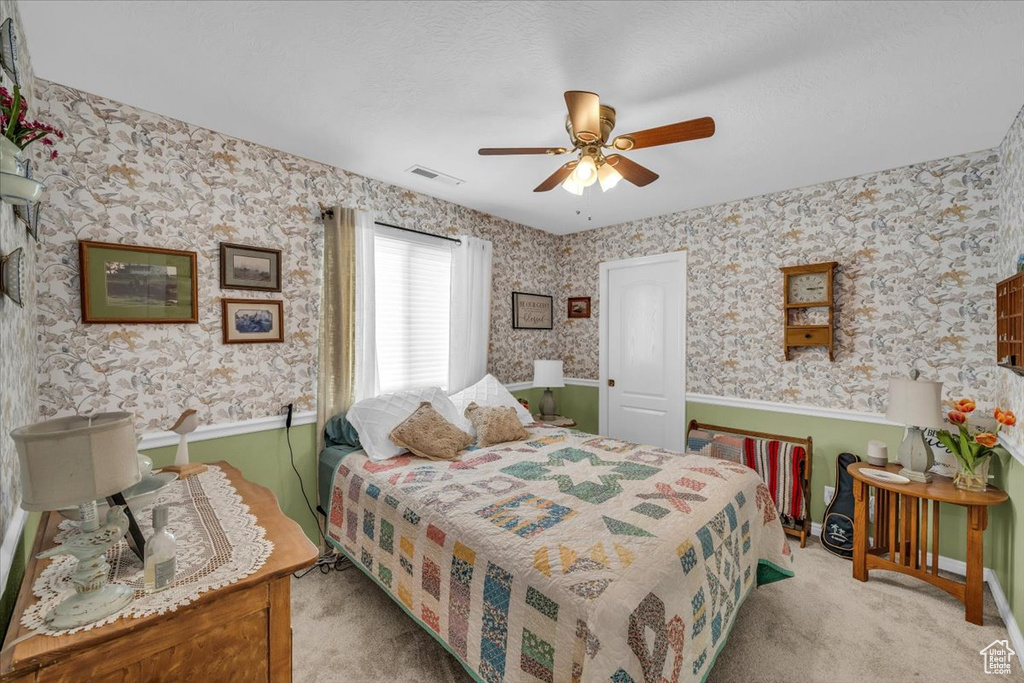 Carpeted bedroom with a ceiling fan, visible vents, and wallpapered walls