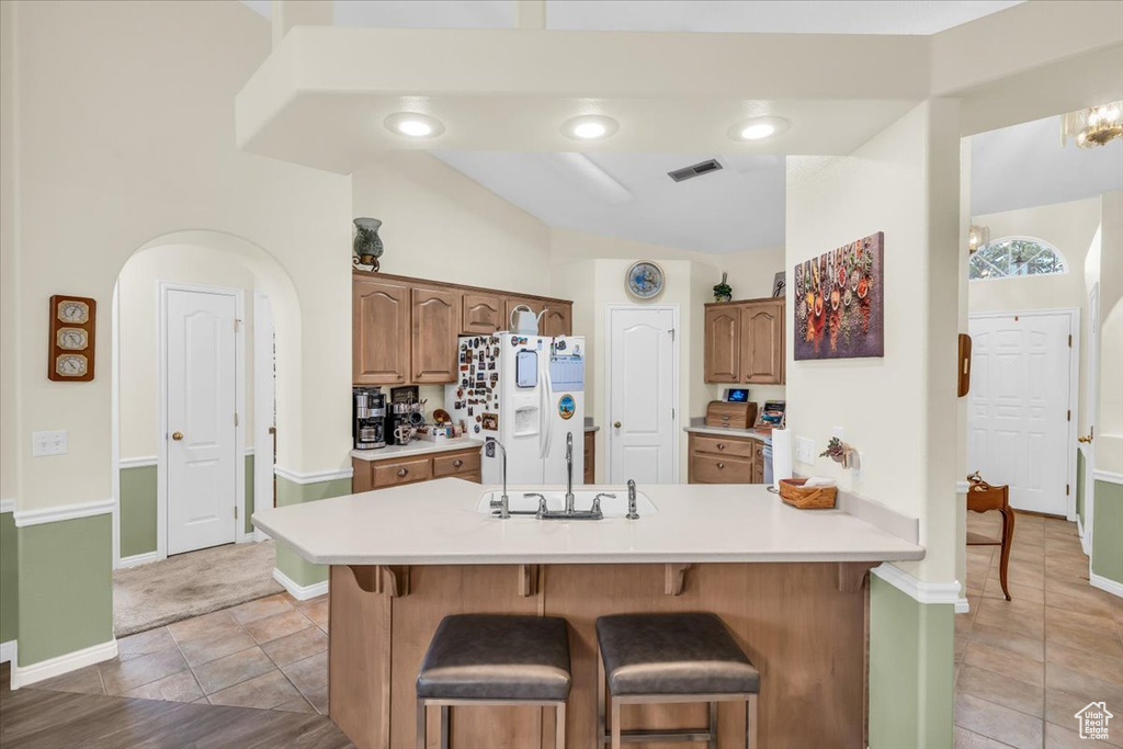 Kitchen with light countertops, white refrigerator with ice dispenser, visible vents, and a breakfast bar area