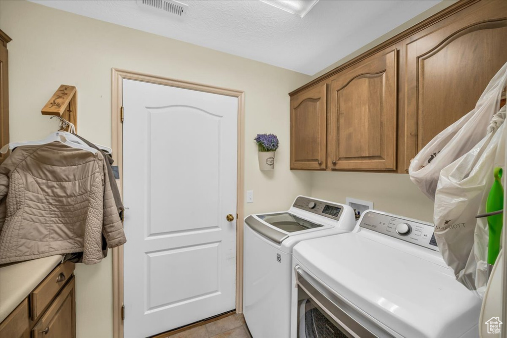 Clothes washing area featuring visible vents, washing machine and dryer, and cabinet space