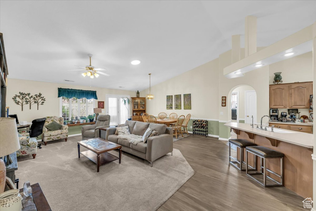 Living room featuring arched walkways, high vaulted ceiling, wood finished floors, a ceiling fan, and baseboards