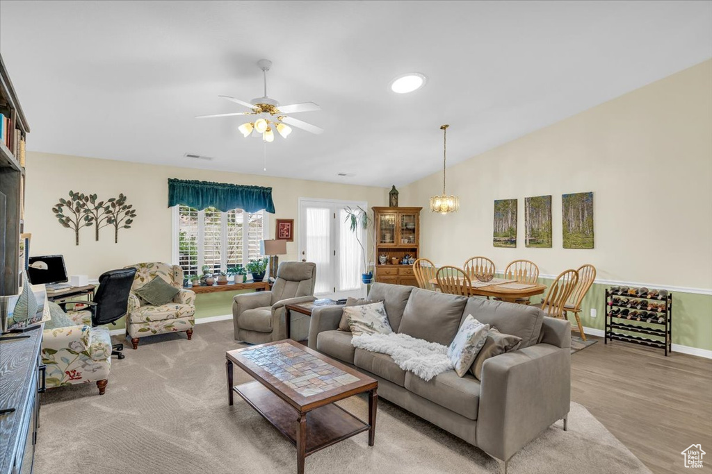 Living area with baseboards, visible vents, light wood-style flooring, vaulted ceiling, and ceiling fan with notable chandelier