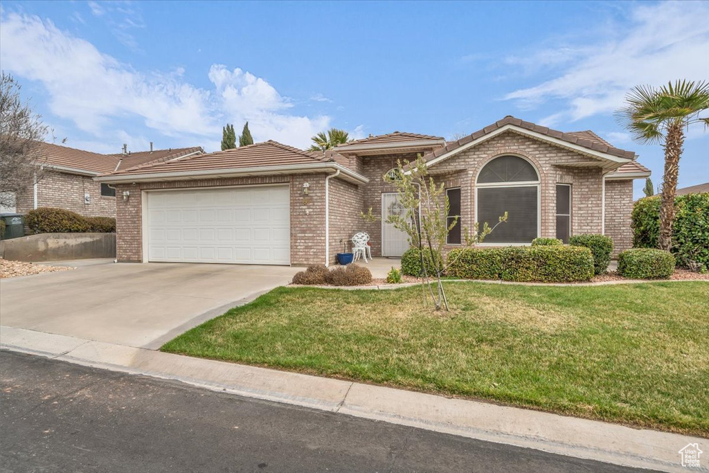 Ranch-style home with concrete driveway, an attached garage, a tile roof, and a front yard