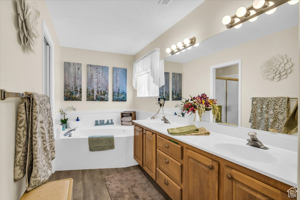 Bathroom with a garden tub, wood finished floors, a sink, double vanity, and a stall shower