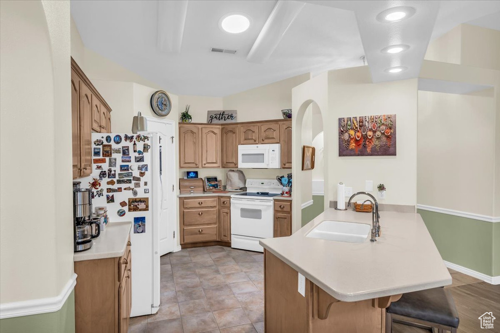Kitchen featuring a peninsula, white appliances, a sink, light countertops, and a kitchen bar
