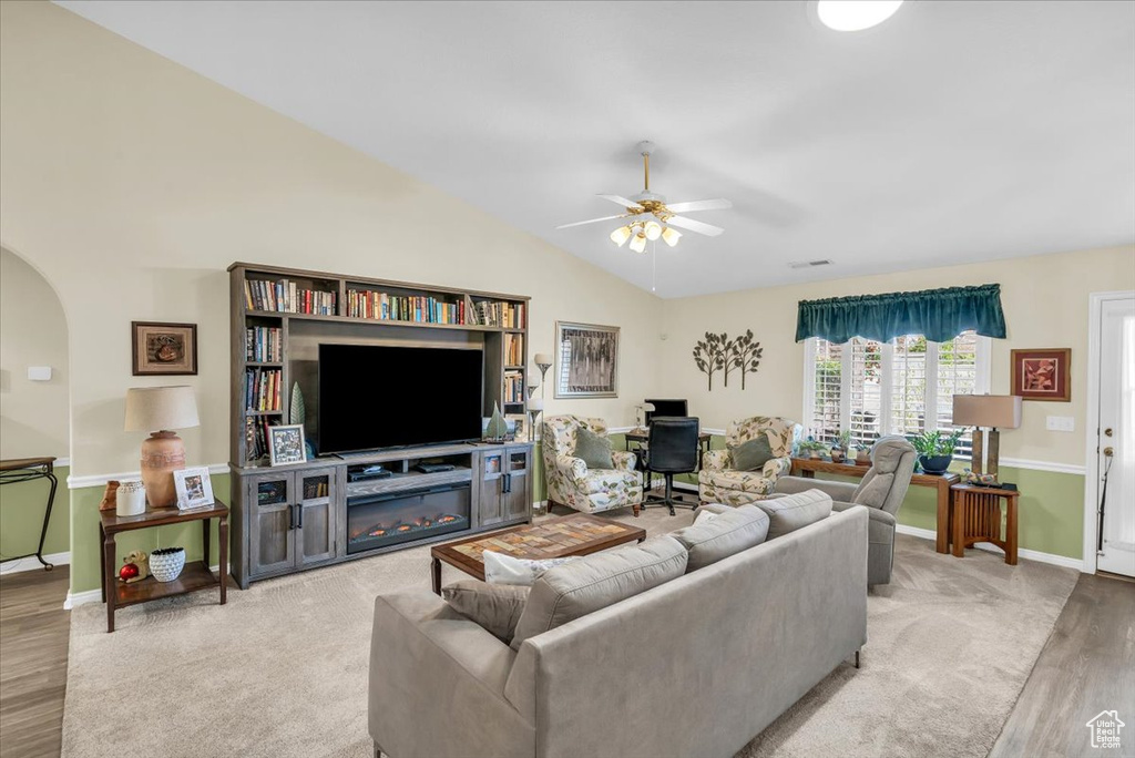 Living room featuring arched walkways, ceiling fan, wood finished floors, vaulted ceiling, and a glass covered fireplace