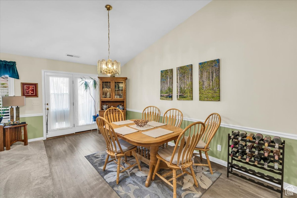 Dining room featuring visible vents, vaulted ceiling, a notable chandelier, and wood finished floors