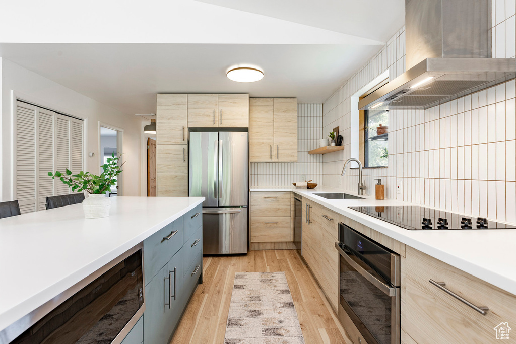 Kitchen with stainless steel appliances, a sink, wall chimney exhaust hood, light brown cabinets, and light wood-style floors