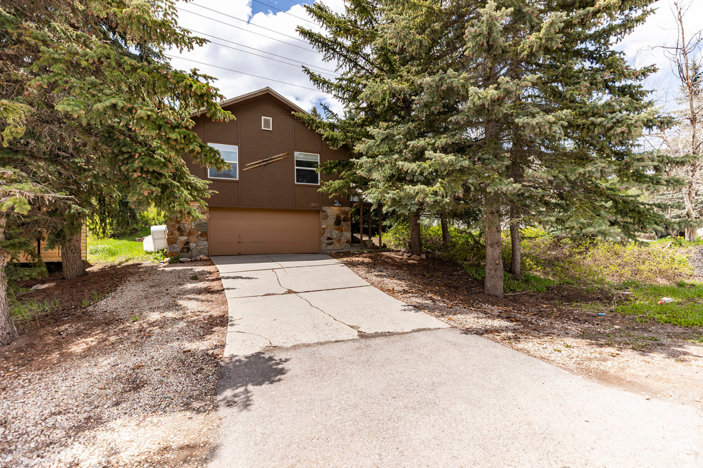 View of front of property featuring an attached garage, concrete driveway, and stone siding