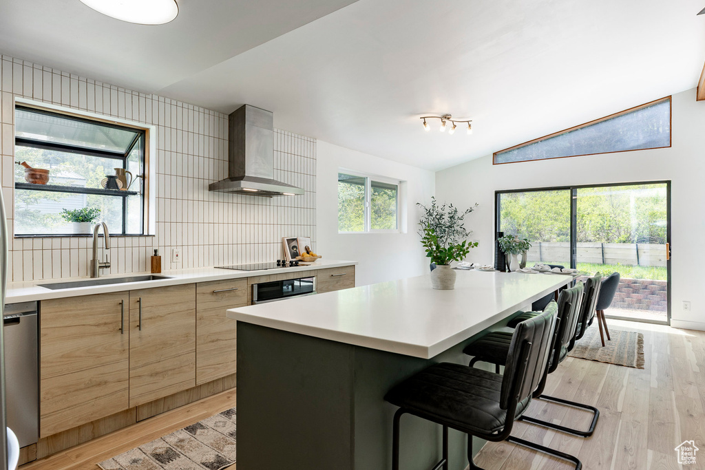 Kitchen with a sink, wall chimney range hood, modern cabinets, light brown cabinets, and light wood-style floors