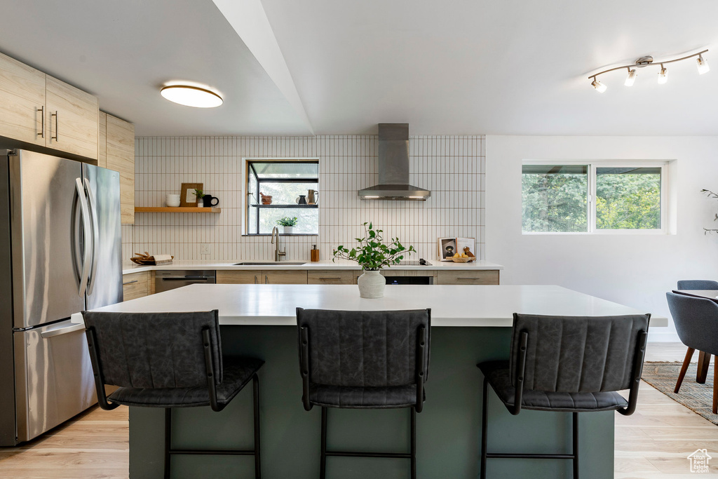 Kitchen with freestanding refrigerator, wall chimney range hood, a sink, and a breakfast bar