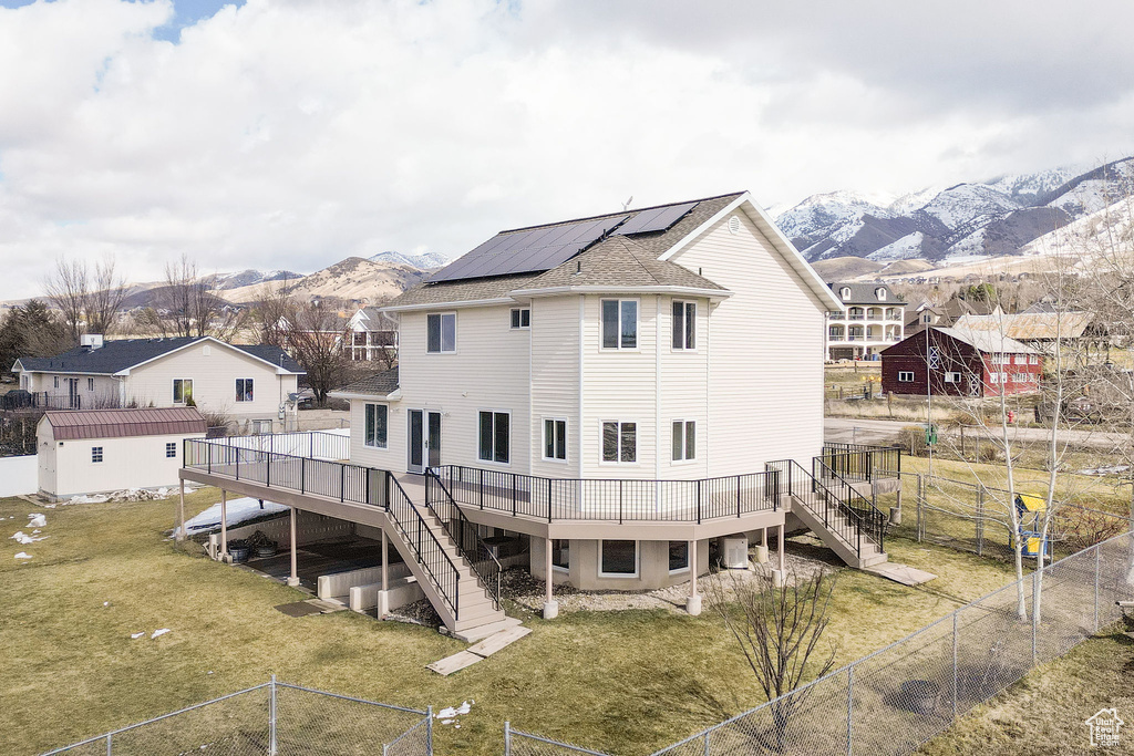 Back of property featuring a deck with mountain view, a fenced backyard, solar panels, stairs, and a yard