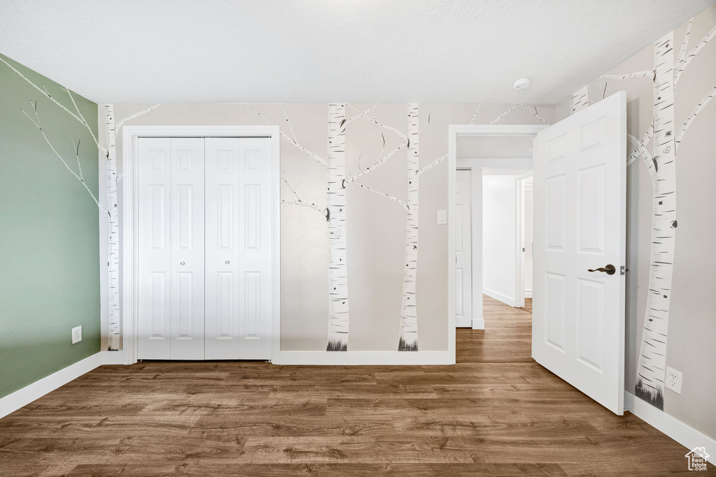 Unfurnished bedroom with a closet, wood finished floors, and baseboards