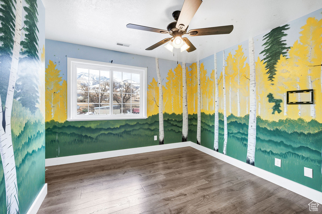 Spare room with a ceiling fan, visible vents, baseboards, and wood finished floors