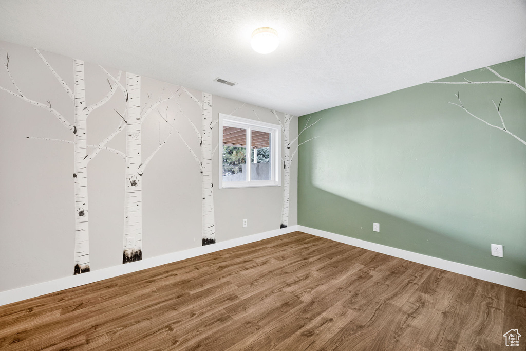 Empty room featuring visible vents, a textured ceiling, baseboards, and wood finished floors