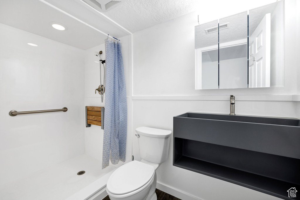 Bathroom featuring toilet, a stall shower, a textured ceiling, and visible vents