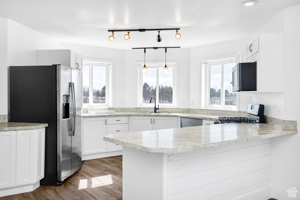Kitchen featuring stainless steel appliances, a peninsula, wood finished floors, a sink, and white cabinetry