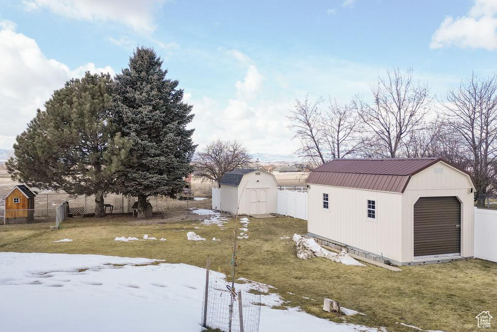 Snowy yard with a storage shed, fence, and an outbuilding