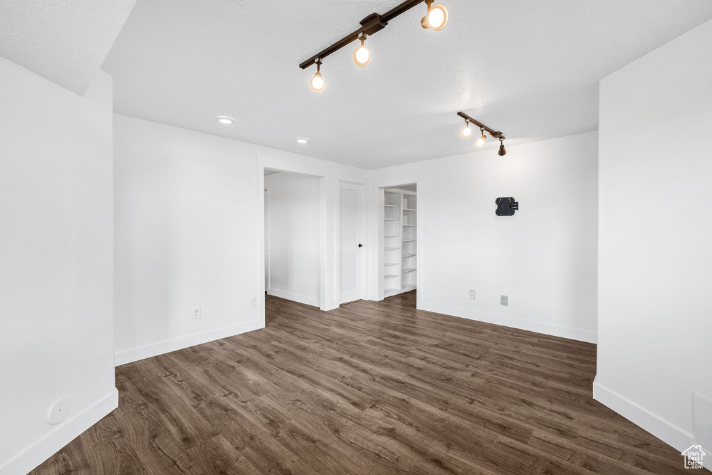 Spare room with dark wood-type flooring, built in shelves, and baseboards