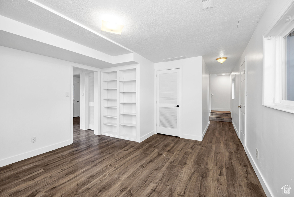 Interior space with built in shelves, baseboards, dark wood finished floors, and a textured ceiling