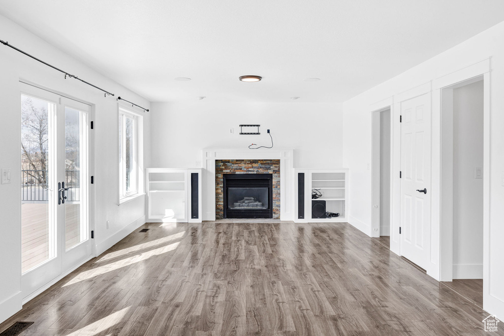 Unfurnished living room featuring baseboards, visible vents, wood finished floors, and a stone fireplace
