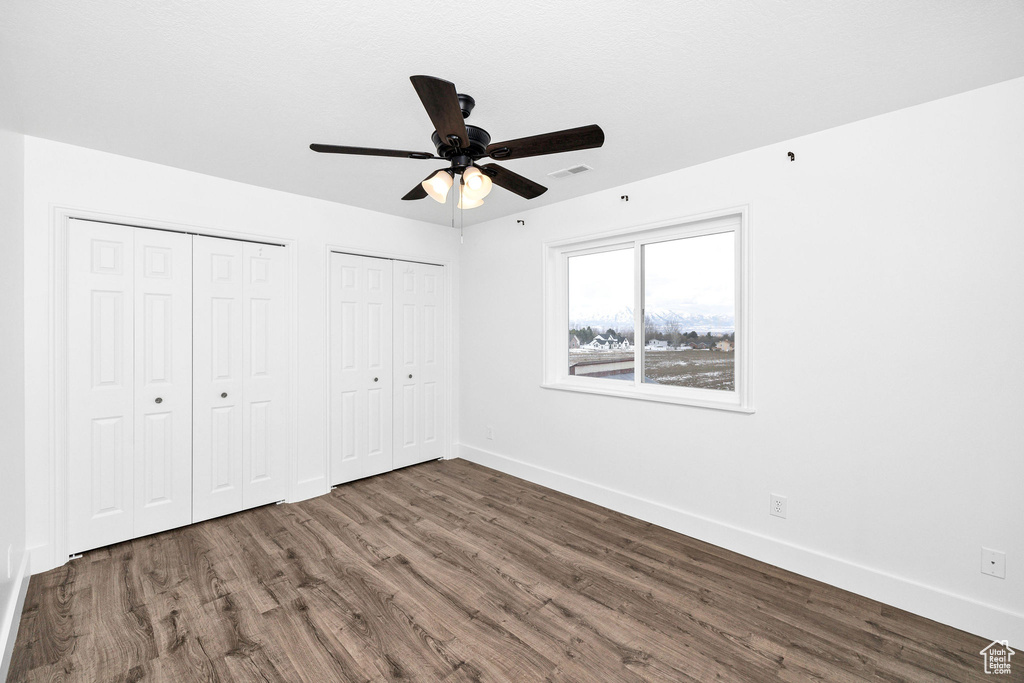 Unfurnished bedroom featuring wood finished floors, visible vents, baseboards, and two closets